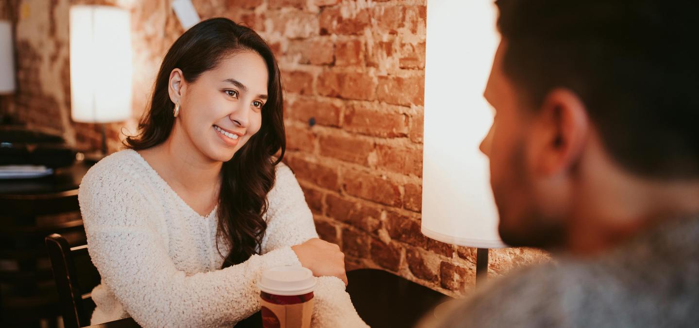 Woman looking at her date in admiration. There's a cup of coffee between them.