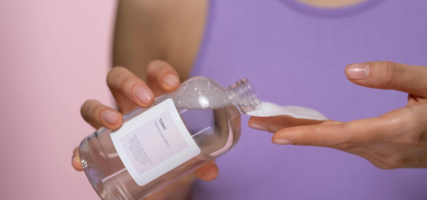 Woman pouring skincare product on a cotton pad.