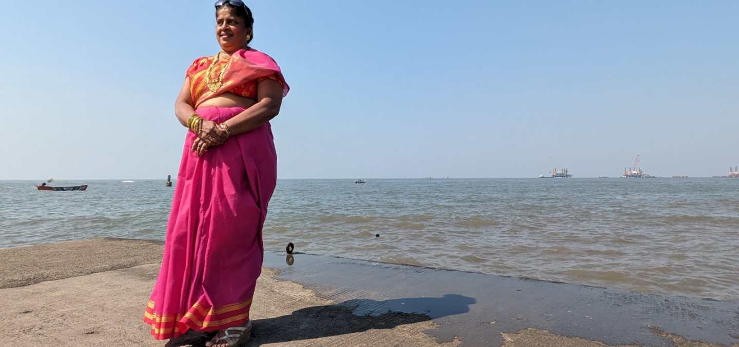 Image of Thelma Falcon, in her red-pink sari posing by the sea shore