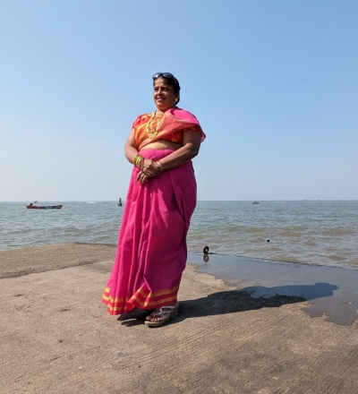 Image of Thelma Falcon, in her red-pink sari posing by the sea shore