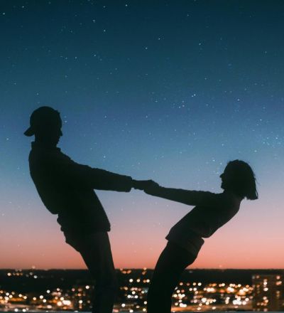 Couple dancing together and holding hands in front of a starry sky. Horoscope for couples as venus enters gemini.