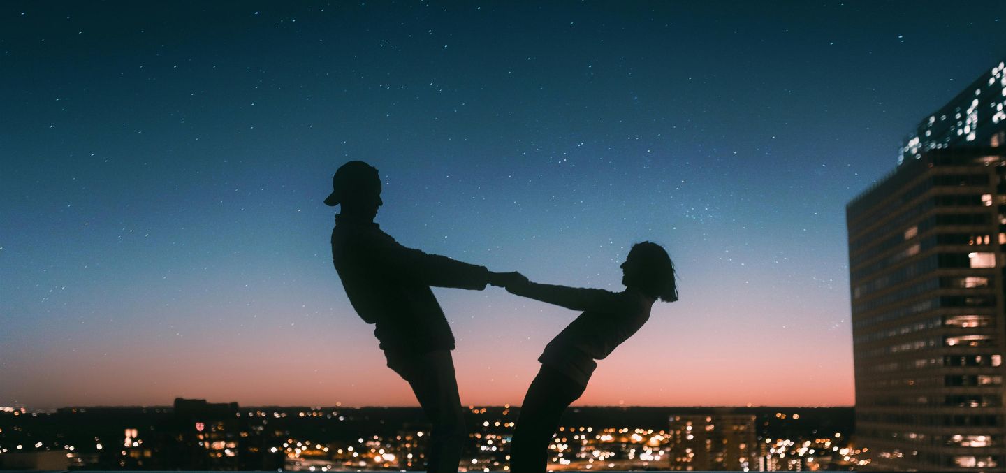 Couple dancing together and holding hands in front of a starry sky. Horoscope for couples as venus enters gemini.