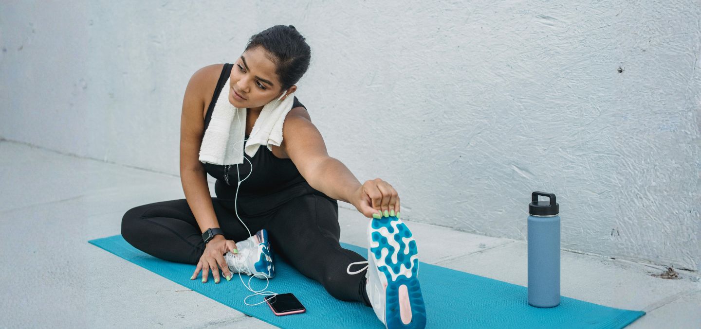 Woman stretching on a blue yoga matt with her water bottle. She's wearing gym wear.