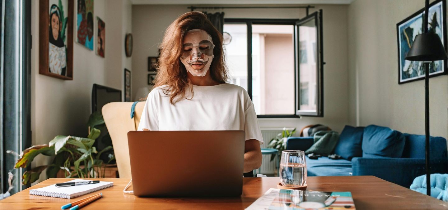 Woman sitting by her desk with a sheet mask on her face.