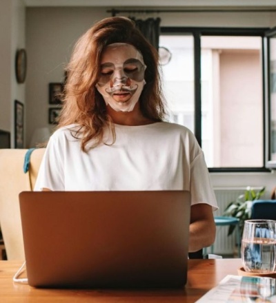 Woman sitting by her desk with a sheet mask on her face.