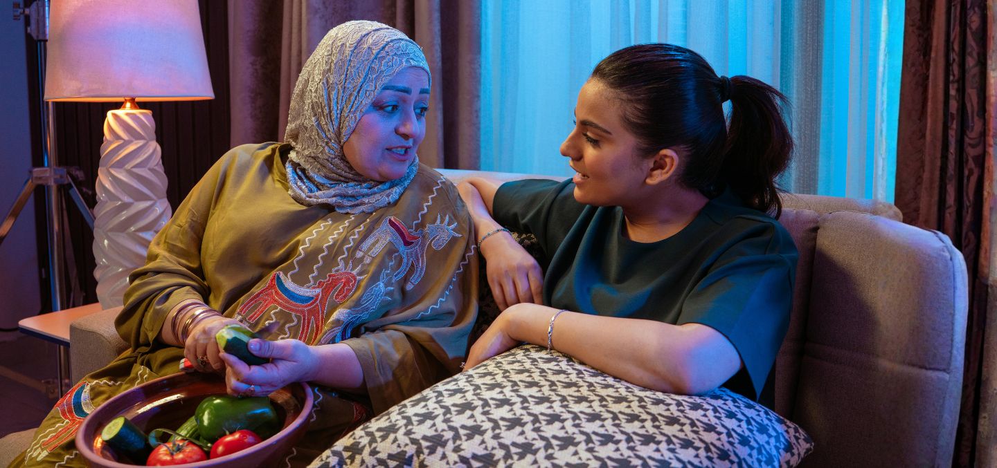 mother and daughter sitting on a cough and mom is cutting vegetables.